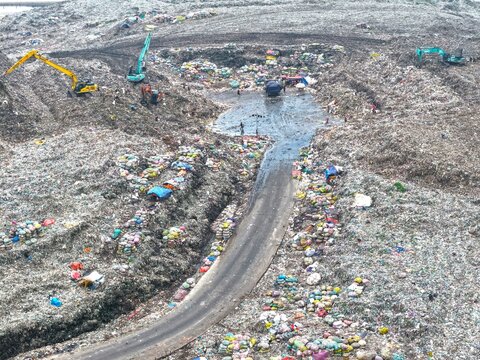 Dhaka, Bangladesh - 27 August 2026: Aerial view of Aminbazar Landfill with heavy machinery excavating waste, piles of garbage, and workers sorting through refuse along a central road.