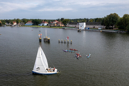Berlin, Germany - 26 August 2026: Aerial view of Berlin-Grunau Regatta Course with a sailboat and kayaks on the Dahme river, surrounded by trees and historic buildings.
