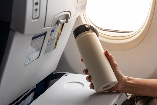 Closeup of passenger hand holding water flask to store hot water during long haul flight for hydration