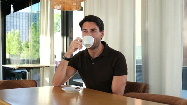 Handsome caucasian man stirring and drinking a cup of coffee while relaxing in a modern cafe