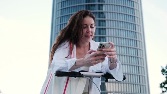 Young woman smiling while using her smartphone with an electric scooter in a modern city