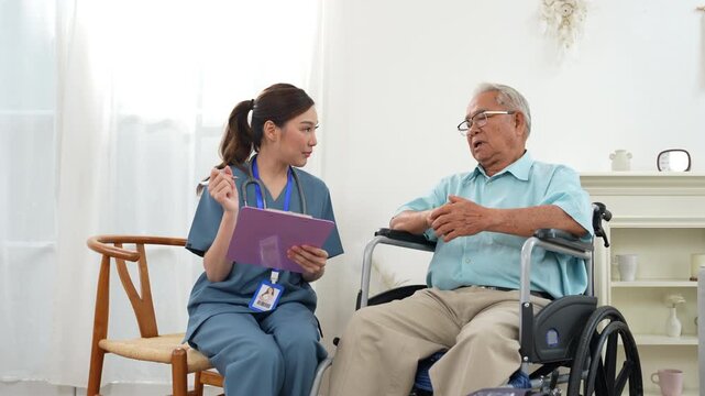 Female nurse assisting an elderly man in a wheelchair during a home healthcare visit, reviewing medical information and discussing care, senior health, nursing, disability support, independence.