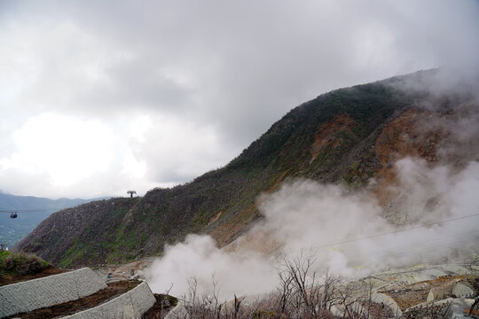 箱根大涌谷の火山活動により噴煙が上がる山肌の風景。ロープウェイが往来し、荒涼とした大地と自然のエネルギーが共存する様子。