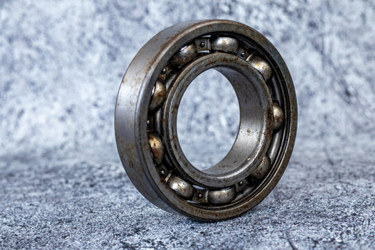 Used steel radial ball bearing standing upright on rough textured concrete workshop floor.