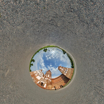 creative tiny planet photo of a rural landscape with dirt road, green fields, and cloudy sky forming a circular world.