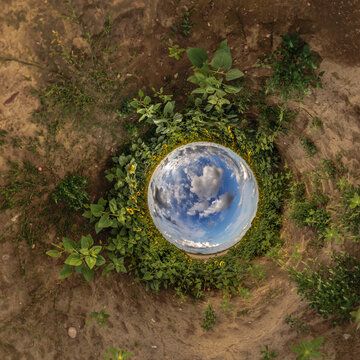 creative tiny planet photo of a rural landscape with dirt road, green fields, and cloudy sky forming a circular world.