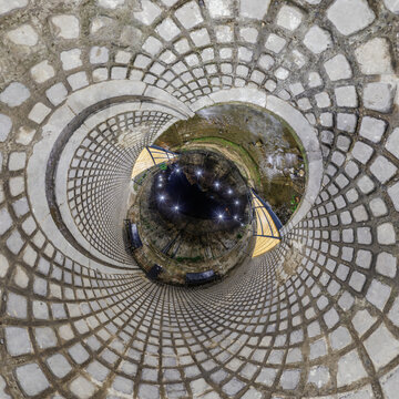 creative tiny planet photo of a rural landscape with dirt road, green fields, and cloudy sky forming a circular world.