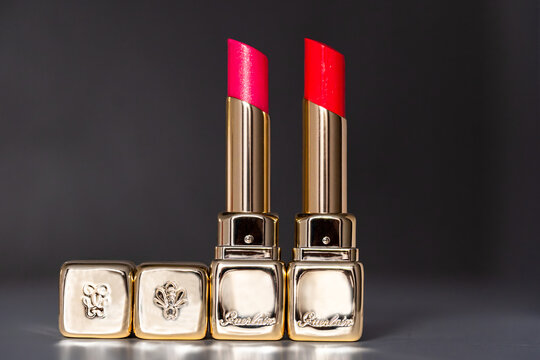 Riga, Latvia - September 05, 2026 - Guerlain Pink and Coral Lip Balms in Gold Cases on Dark Background with Copy Space
