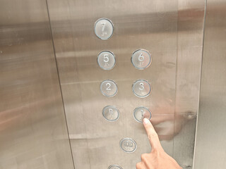 a hand pressing the number one button on a stainless steel elevator control panel with braille. © Hendri3738