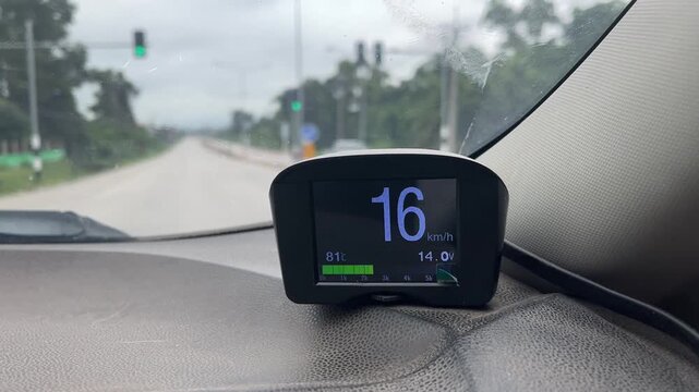 In-Car Speedometer Display: A digital heads-up display unit mounted on a car's dashboard shows the vehicle's speed as 16 km/h. The display also shows battery status and other driving information.