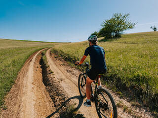 Fototapeta premium A lone mountain biker riding along a dirt path through peaceful meadows in Gemer, Slovakia.