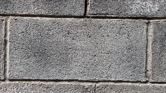 Cinder Block Wall Texture: A close-up, detailed view of a rough, grey cinder block wall, showcasing its gritty texture and the mortar lines that bind the construction elements together.