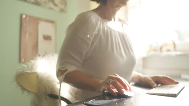 Middle aged woman working at home office desk with computer mouse and keyboard.