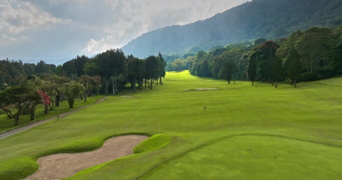Golf course fairway winding through tropical trees with mountains in the background. Bali island active sports and recreation. Aerial drone flight