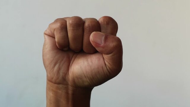 A human hand held up in a tight fist against a plain background.