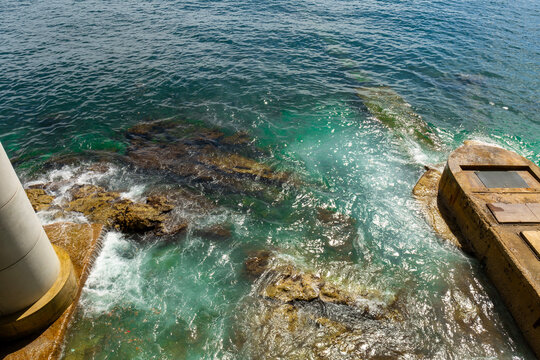 Aerial top-down view of rocky shoreline where the waves are dramatically crashing against the rocks and stones
