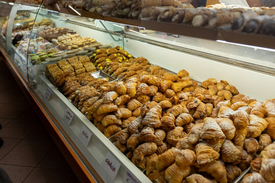 A tempting window display of stacked Cannoli pastries in Sanremo, featuring classic, pistachio, and amaretto flavors, with handwritten price tags showcasing Italian street food.