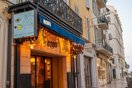 Cannes, France - August 03, 2026: Storefront of Bobo Bistro Vivant illuminated with warm lights along a street with shops and balconies