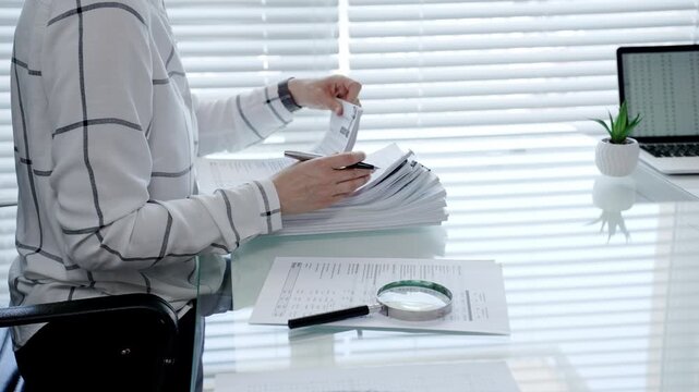 Professional woman categorizing important business documents and financial statements on an office desk. Managing a stack of files during a detailed audit