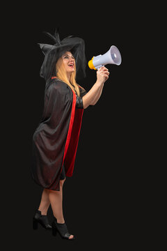 Woman dressed in a witch costume with a black hat and cape, smiling while holding a megaphone and shouting, symbolizing communication, announcement, celebration, and fun for Halloween