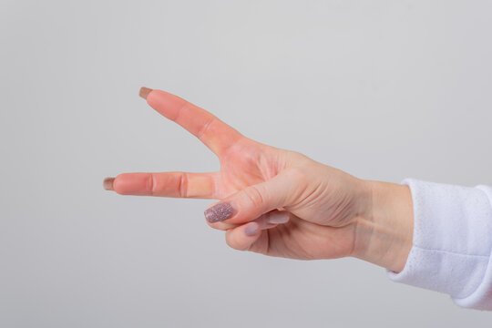Female hand with manicured nails displaying a symbol of peace or victory, extending two fingers against a clean, light grey background, conveying a positive message