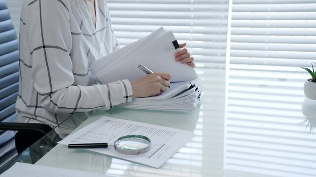 Professional woman categorizing important business documents and financial statements on an office desk. Managing a stack of files during a detailed audit