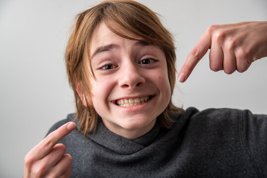 Cheerful young boy with a broad smile pointing at himself with both index fingers, expressing confidence, happiness, and self identification on a bright background
