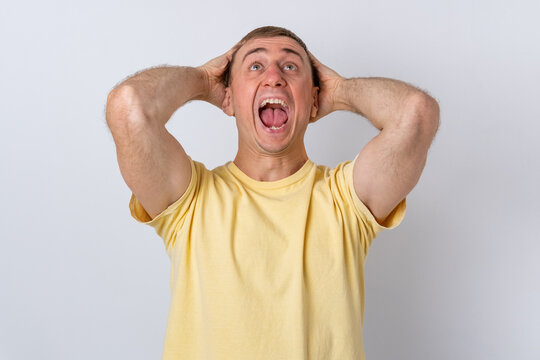 Stressed man screaming with hands on head, experiencing extreme panic and fear, feeling overwhelming frustration, anxiety, and despair on a light background