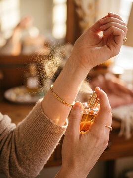 Woman spraying luxury fragrance mist onto her wrist in warm golden light