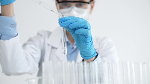 Scientist in protective gear performing a critical laboratory experiment, carefully transferring liquid with a pipette into a test tube during medical research and development