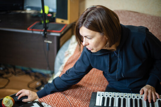 Creative woman working in home music studio with synthesizer and computer