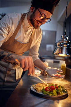 Cook in Professional Modern  kitchen, restaurant concept. chef decorating meal in dramatic lighted kitchen.