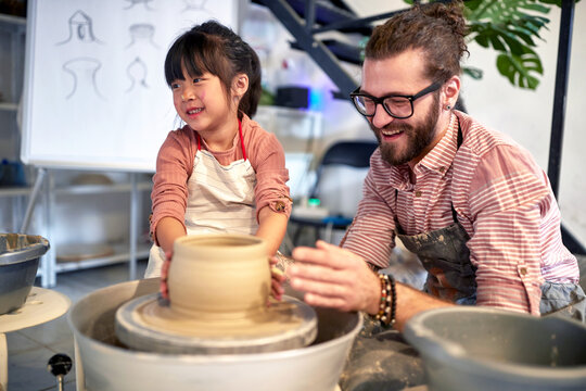 happy child making handmade pot from clay with teacher in pottery school. Creative, hobby ,workshop  concept