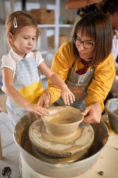 Student girl and teacher shaping pot from clay on a wheel at pottery workshop.  Creative, hobby ,workshop  concept