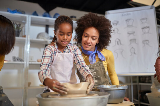 smiling Teacher molding a clay pot with a girl on a pottery workshop.  Creative, hobby ,workshop  concept