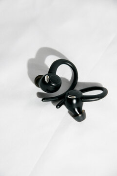 Pair of black true wireless sports earbuds with ear hooks casting shadows on a white fabric background