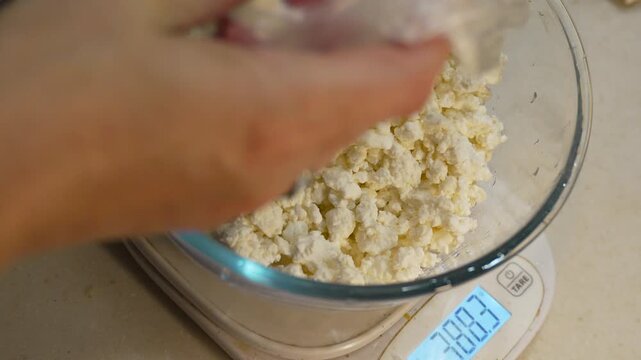 Cottage cheese measuring, kitchen scene shows fresh curds poured onto a digital scale for precise weight. High-angle close-up shot.