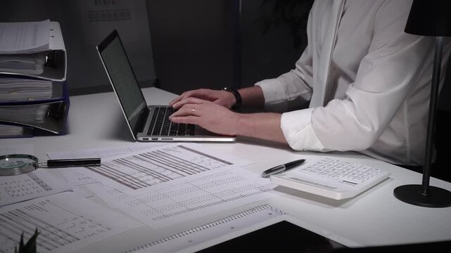 Dedicated finance professional at a cluttered desk, focused on analyzing documents and numbers with laptop, calculator and magnifying glass while managing company records and budgets