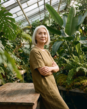 Serene mature woman standing among tropical plants in glass greenhouse