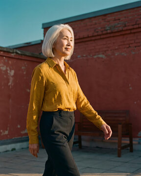 Determined mature woman walking across rooftop terrace past brick wall