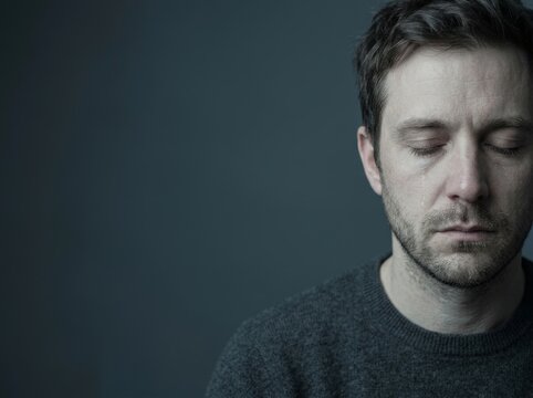 A close-up portrait of a solemn man with a tear, against a gray backdrop.