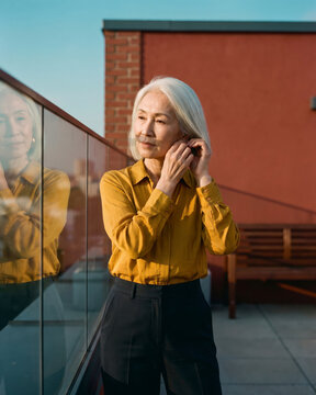 Confident mature woman adjusting earring on sunlit rooftop terrace with warm natural light