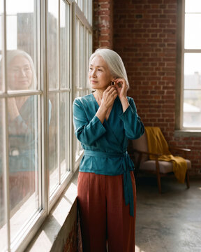 Thoughtful mature woman gazing out large window inside industrial loft