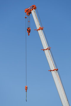 Four-section telescopic crane boom extending upward against a clear blue sky, suspending a main hoist and whip line from an orange tip.