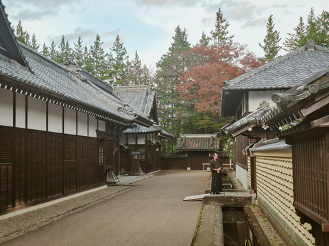 Nikko, Japan - 29 August 2026: View of a man in traditional attire standing in the historic temple complex of Nikko, surrounded by wooden buildings with tiled roofs and trees.