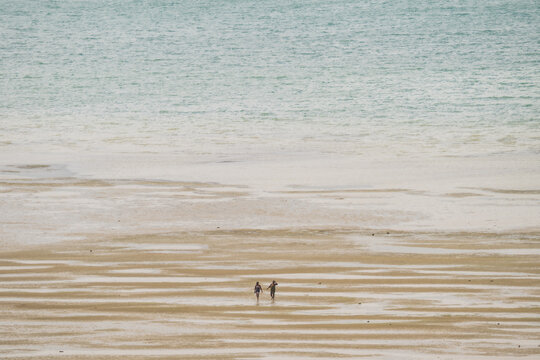 Antsiranana, Diana, Madagascar - 15 June 2026: View of two people walking across the vast, wet sand of a beach at low tide with the calm ocean in the background.