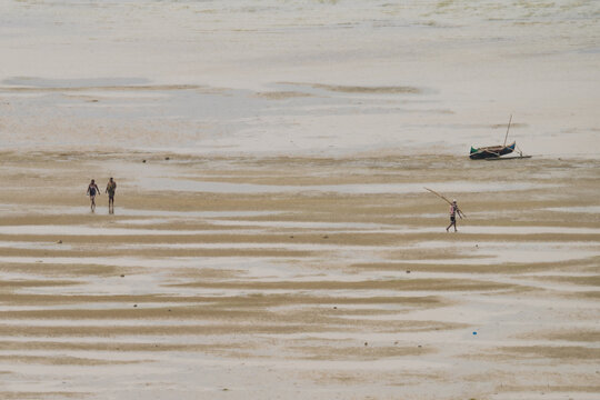 Antsiranana, Diana, Madagascar - 15 June 2026: View of a sandy beach at low tide with people walking across the rippled shore near a traditional wooden boat.