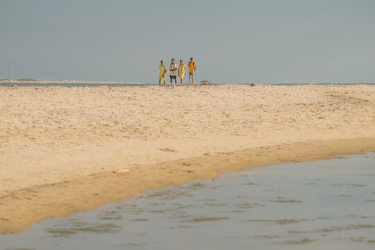 Morondava, Menabe, Madagascar - 29 June 2026: View of four people walking along the sandy beach with calm water under a clear sky.