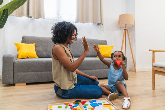 Happy african american mother and toddler daughter bonding while playing with colorful blocks, sharing a high five at home