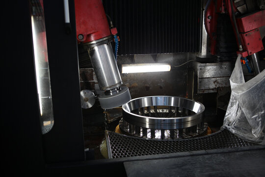 Bearing production. Close-up of grinding machine processing steel ring. Red frame, silver spindle, abrasive head. Dark industrial background. Precision manufacturing